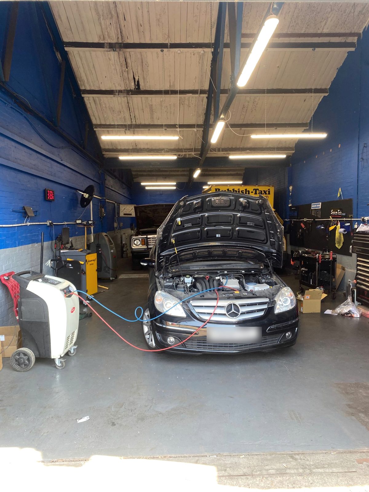 A car with its bonnet up, connected to workshop equipment